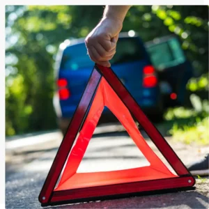 Hand placing a red reflective warning triangle on the roadside behind a stopped blue vehicle.